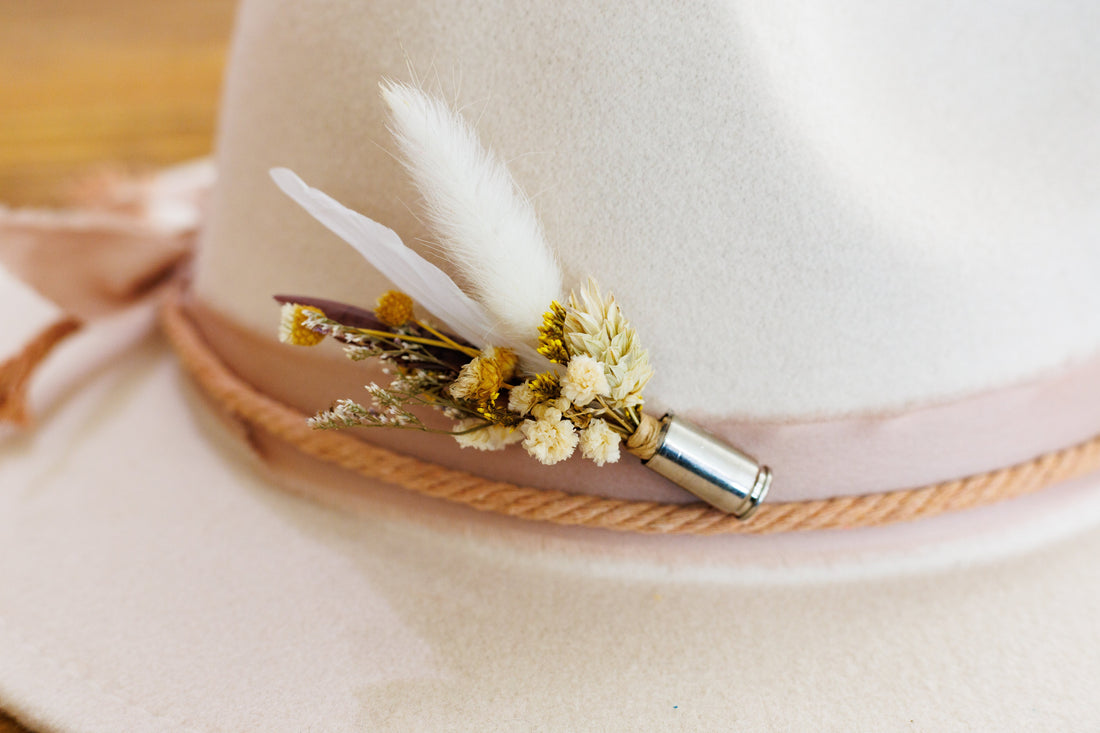 bridal floral hat pin with neutral feathers and flowers encased in a bullet casing on a cream wide brimmed hat