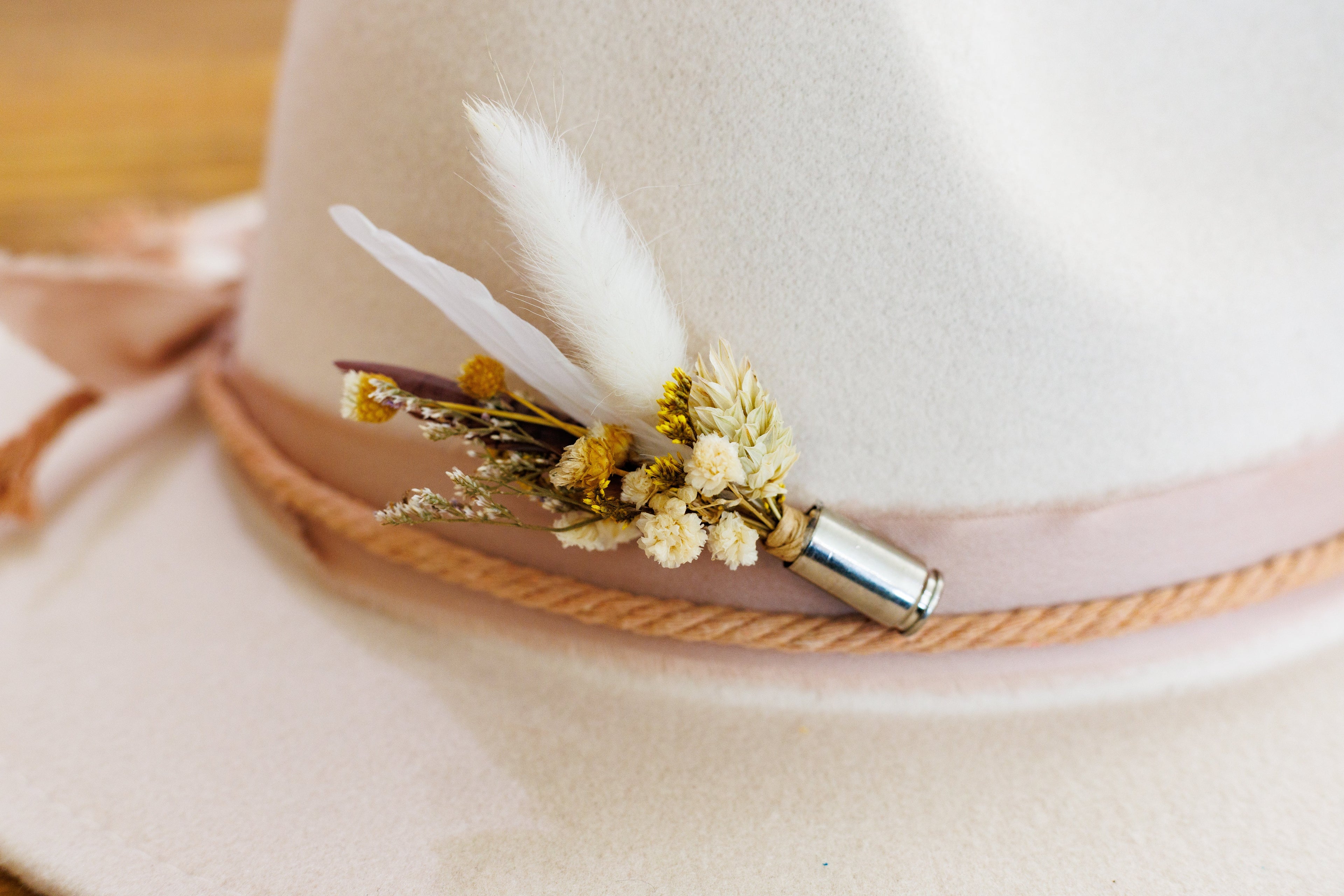 bridal floral hat pin with neutral feathers and flowers encased in a bullet casing on a cream wide brimmed hat