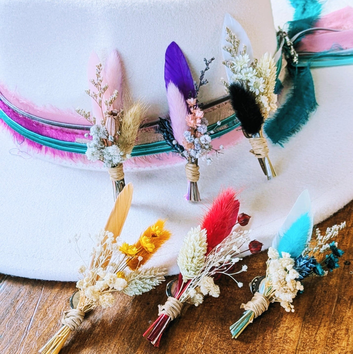 Six BittyBud hat pins in assorted colors arranged on a white felt hat with a pink, magenta, and teal ribbon band