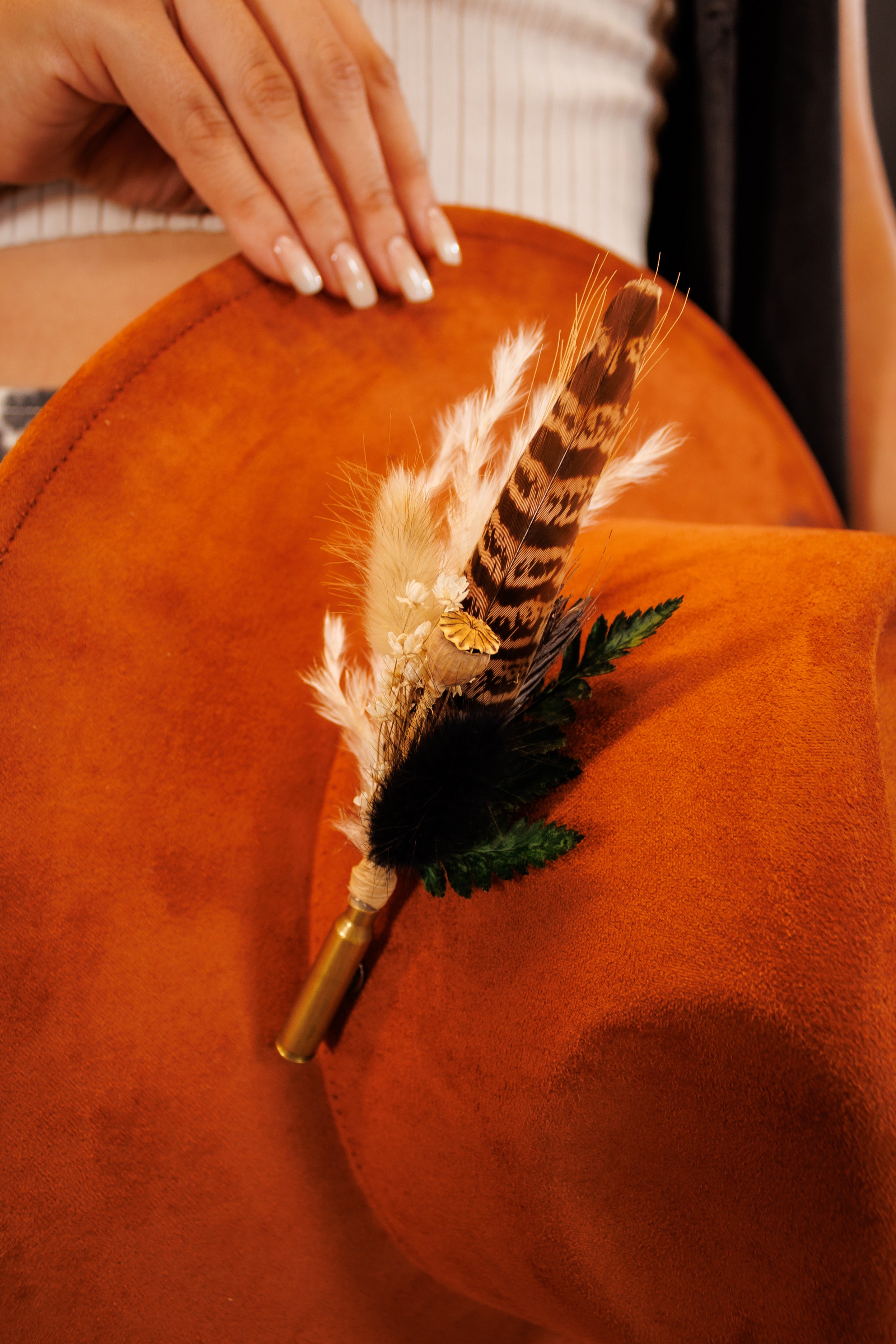 Feathered decorative item on a textured orange surface with a hand in the background.
