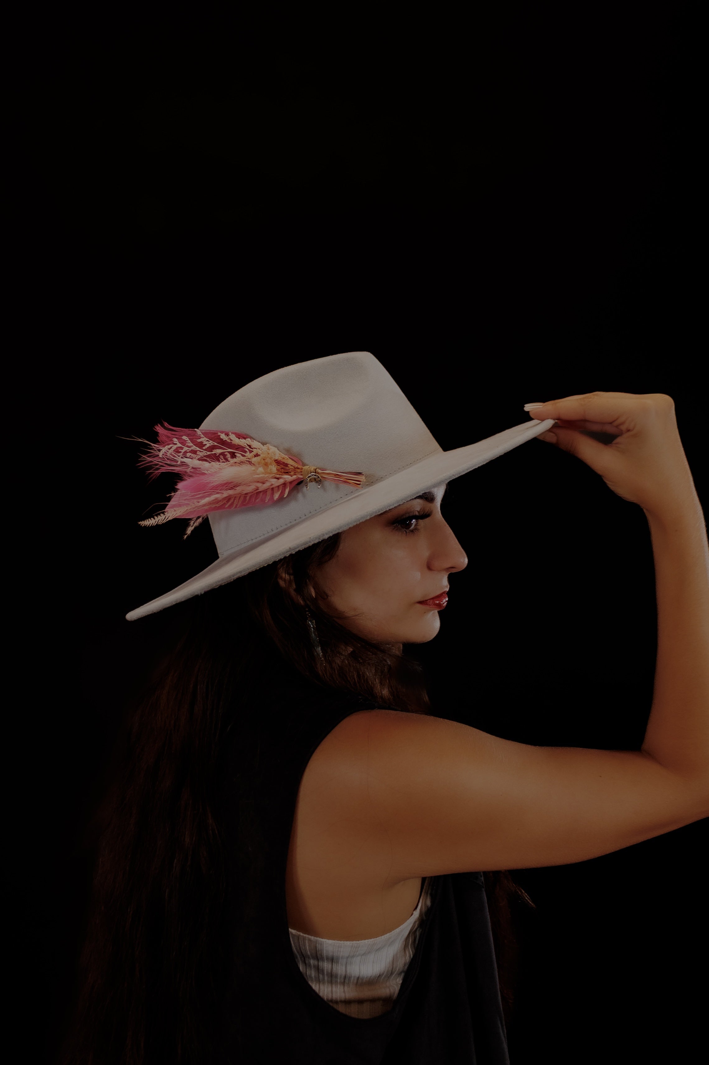 Woman wearing a white hat with pink feathers against a black background