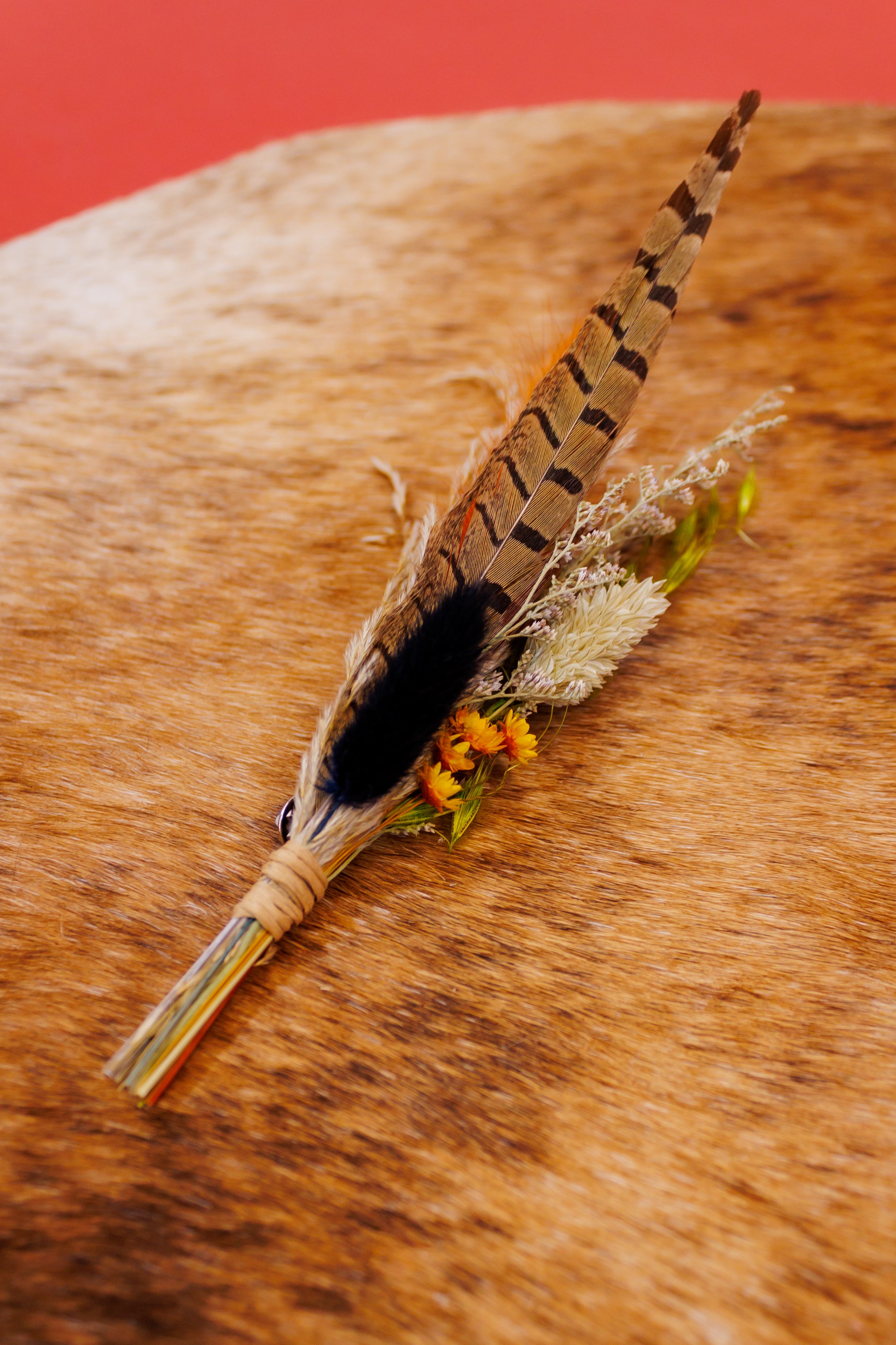 Feather boutonniere on a wooden surface with a red background