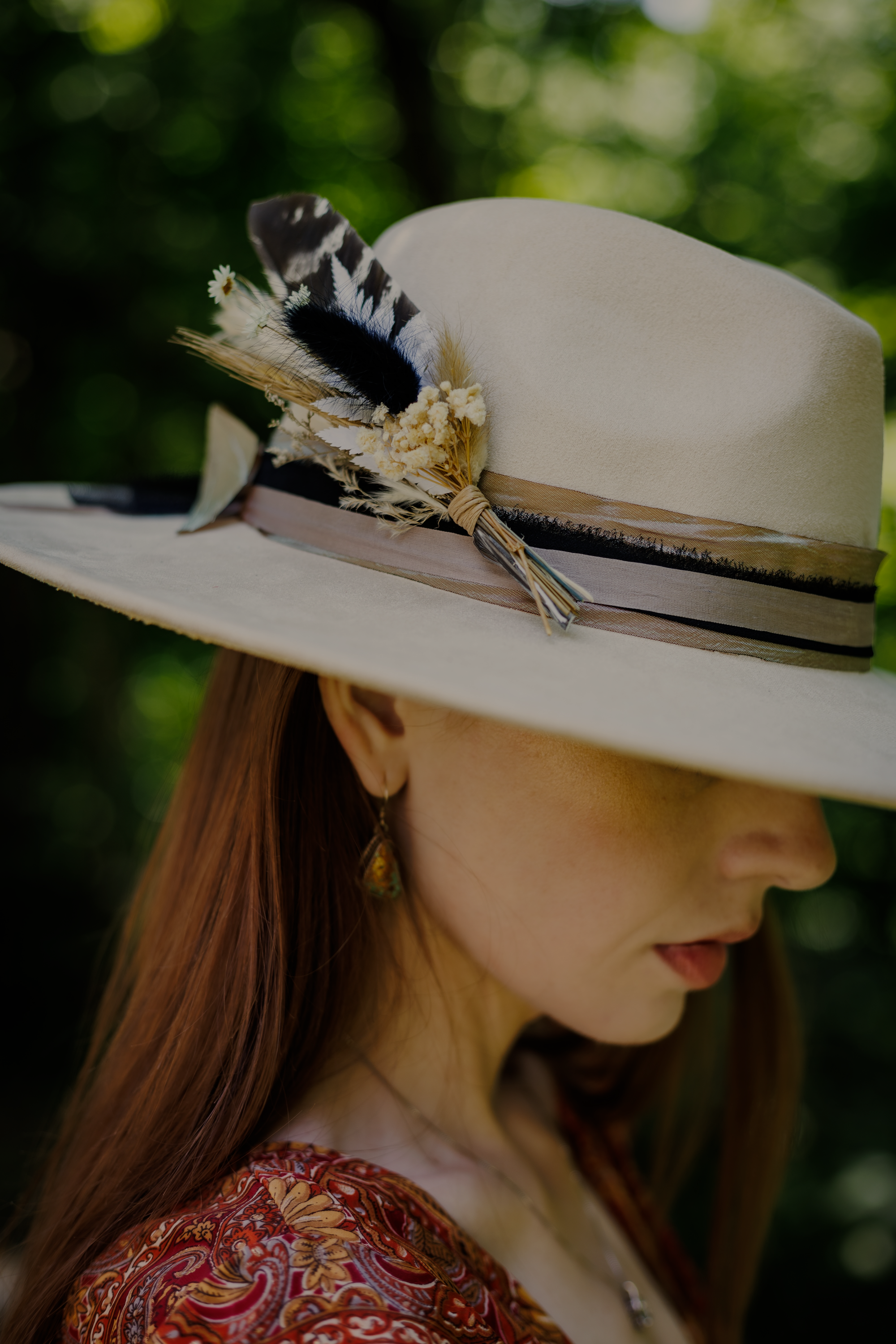 Person wearing a wide-brimmed hat with feather decorations against a blurred green background
