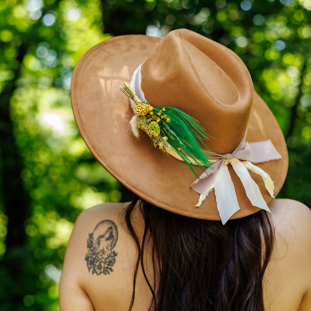 Person wearing a tan hat with decorative elements against a green forest background