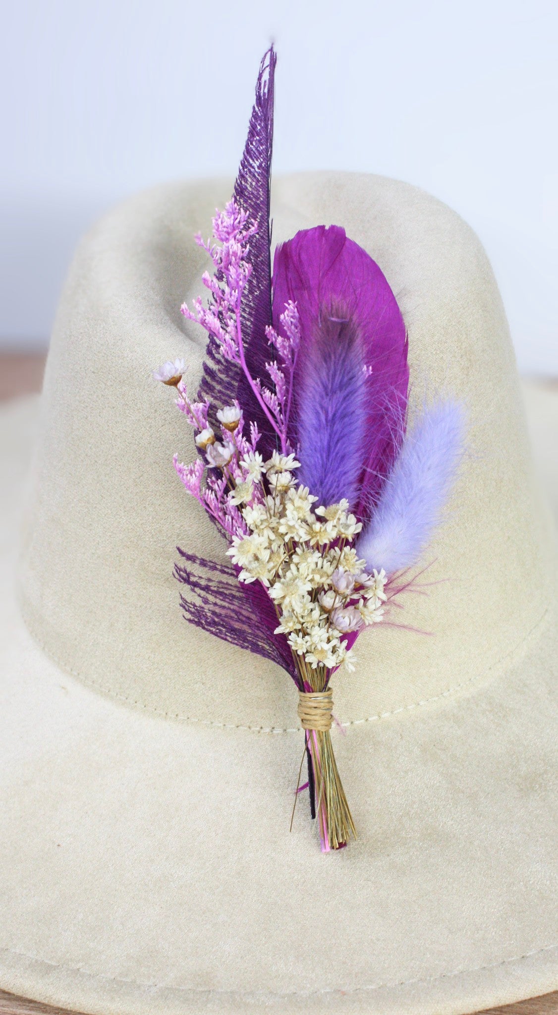 A dried flower and feather hat pin featuring vibrant purple feathers, light purple pampas grass, and small beige dried flowers. 