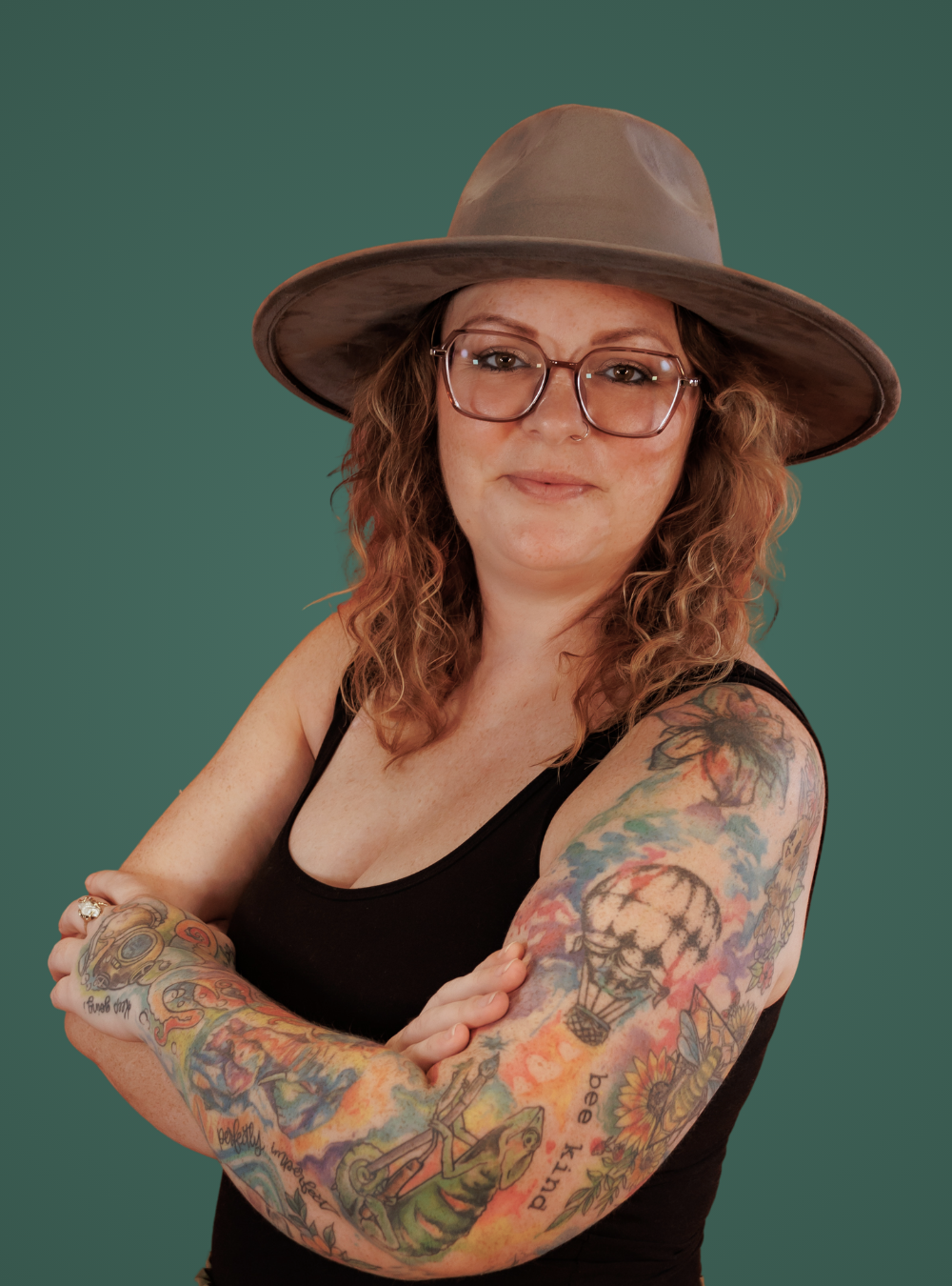 Woman with tattoos on arms wearing a brown hat against a green background