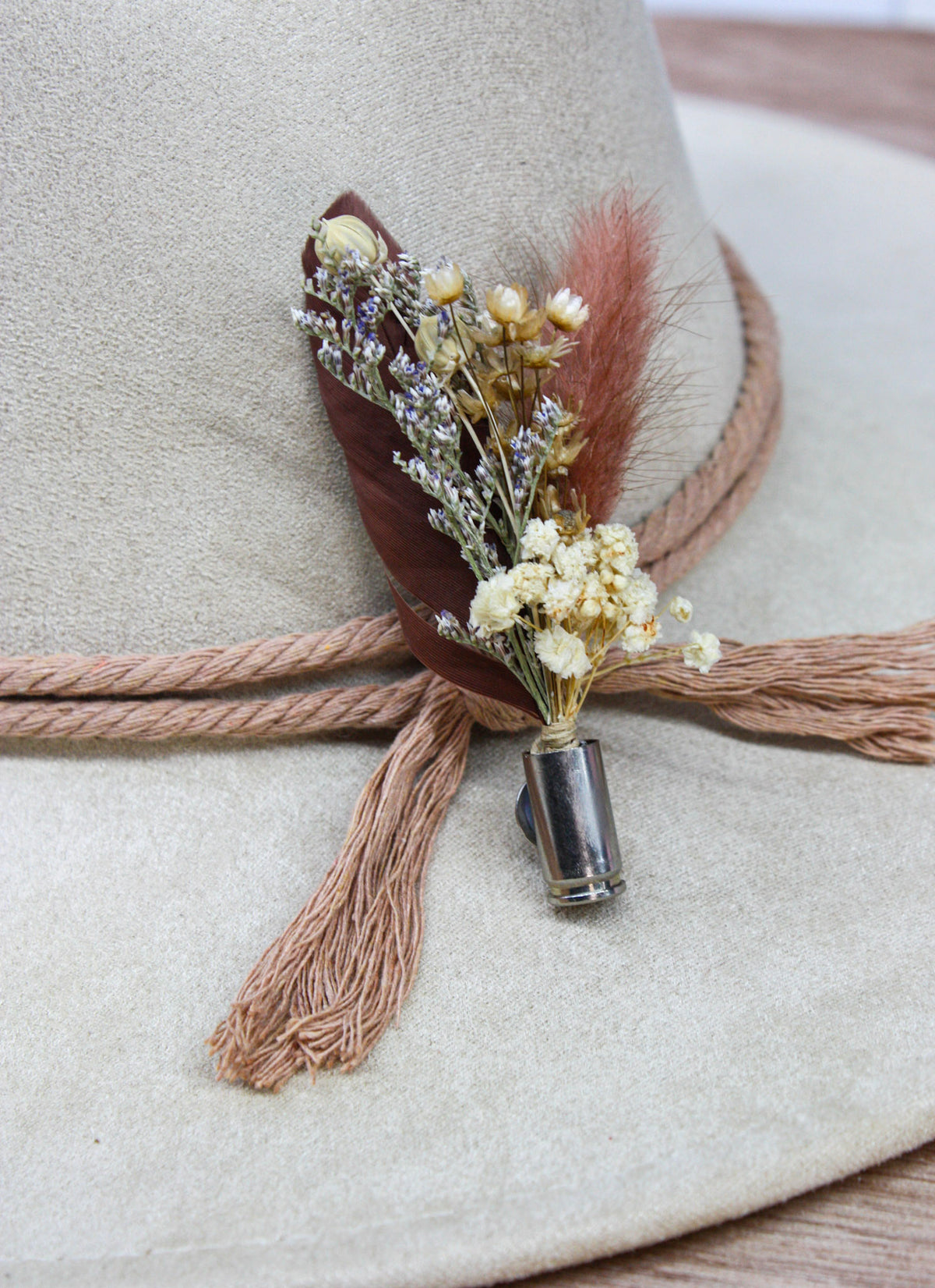 A close-up of a beige wide-brim hat with a decorative brown rope band and a feathered floral hair accessory pinned at the front.