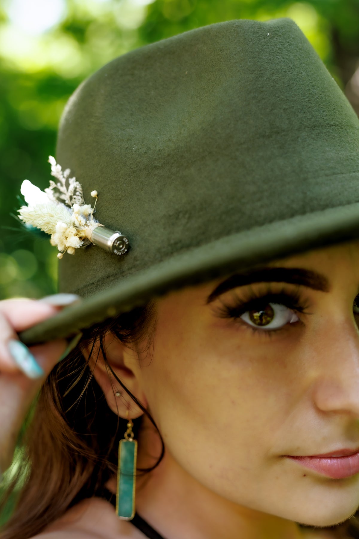 Woman wearing a green hat with decorative mini pinny elements, outdoors.