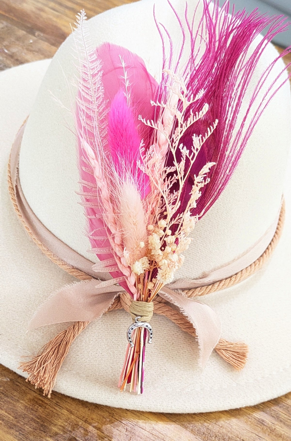 Premium Pink Pony Club BrimBud hat pin with hot pink feathers, blush florals, and silver horseshoe charm on a cream felt hat