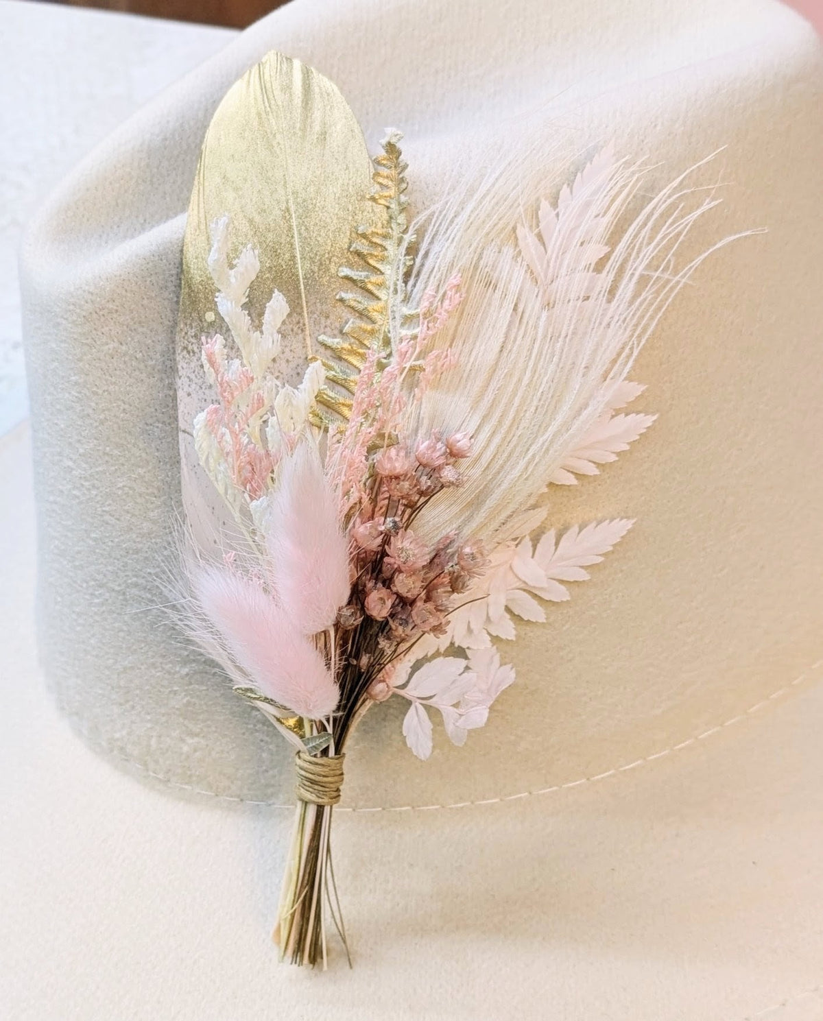 Premium BrimBud hat pin The Dolly with gold feather, blush pink florals, and white fern accents on a cream felt hat