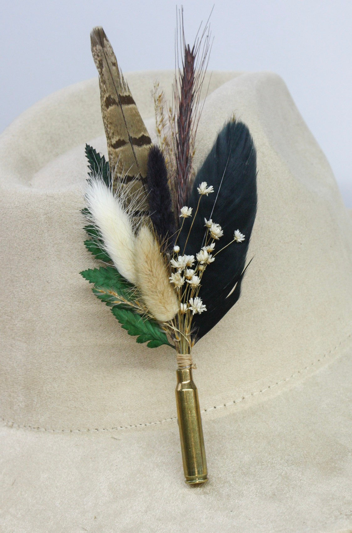 Bullet BrimBud hat pin Umber with barred brown and black feathers, cream bunny tails, and green fern on a cream felt hat